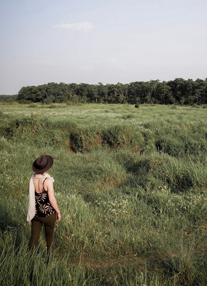 Monica in tall green grass, watching a rhino from afar in May - one of the best seasons in Nepal for wildlife.